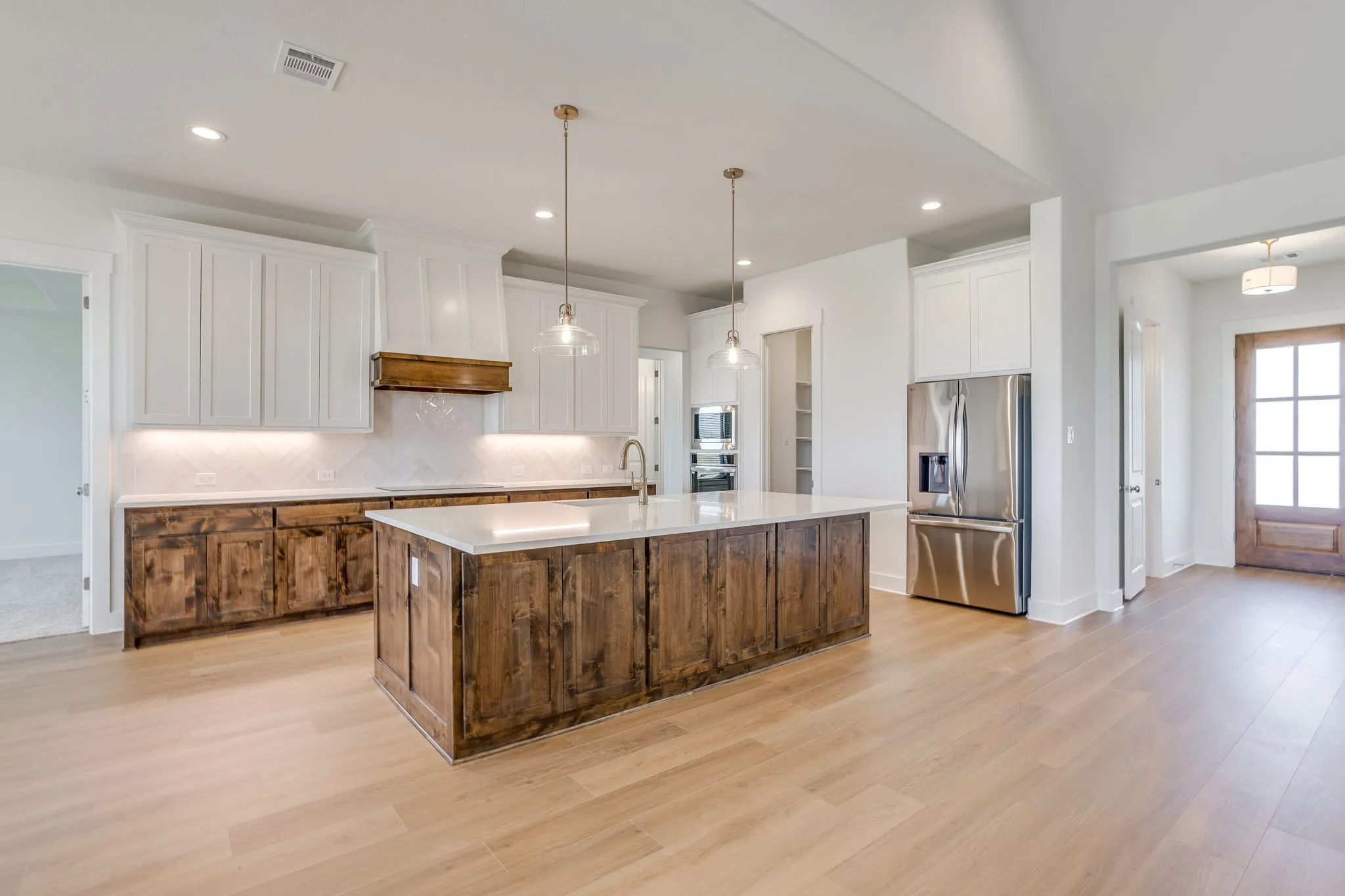 Kitchen featuring dual-toned cabinetry, a spacious center island with a light-toned countertop, stainless steel appliances, and wood-finish flooring