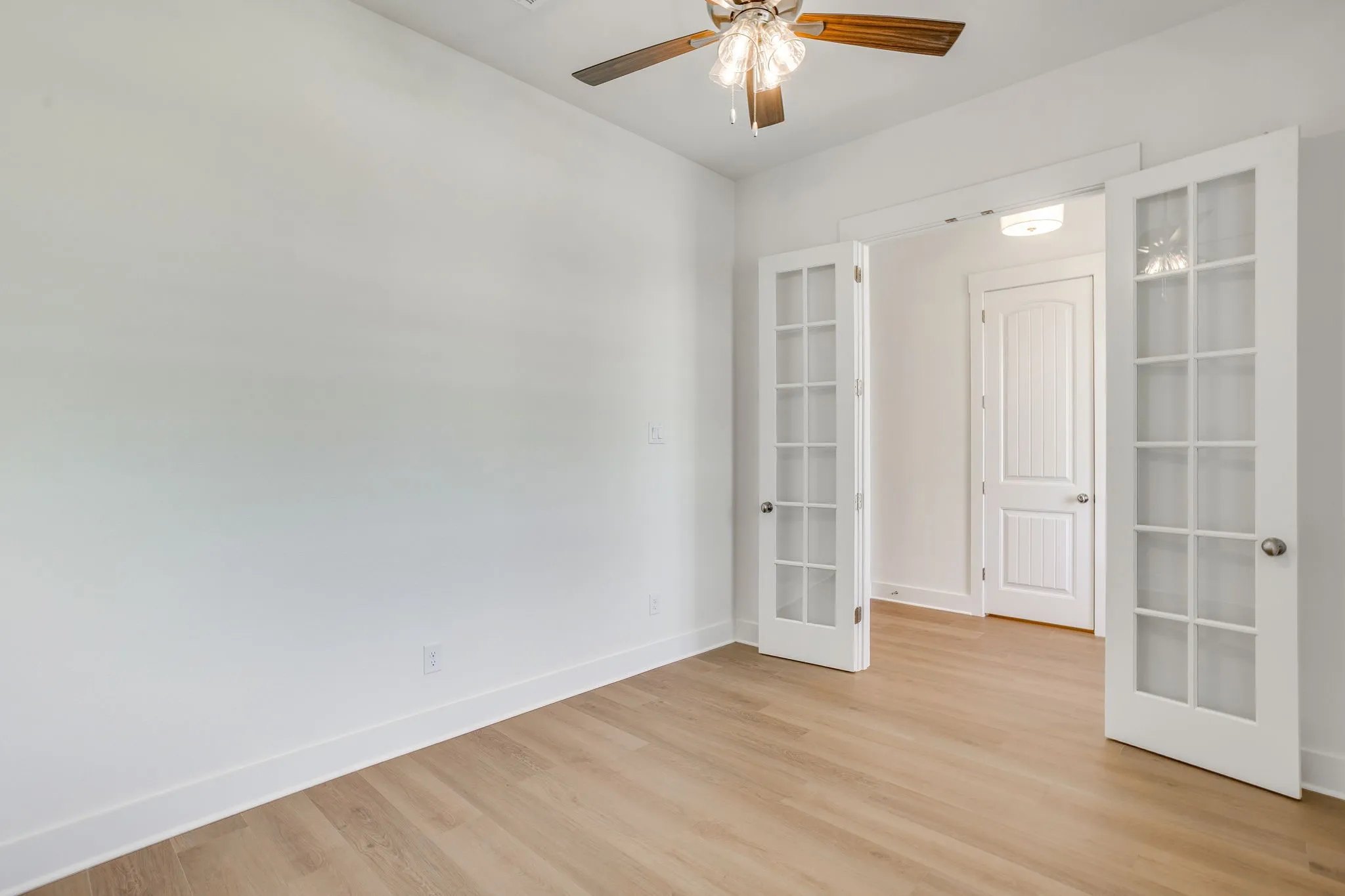 Wood-finish flooring, white walls, double French doors, ceiling fan, and overhead lighting
