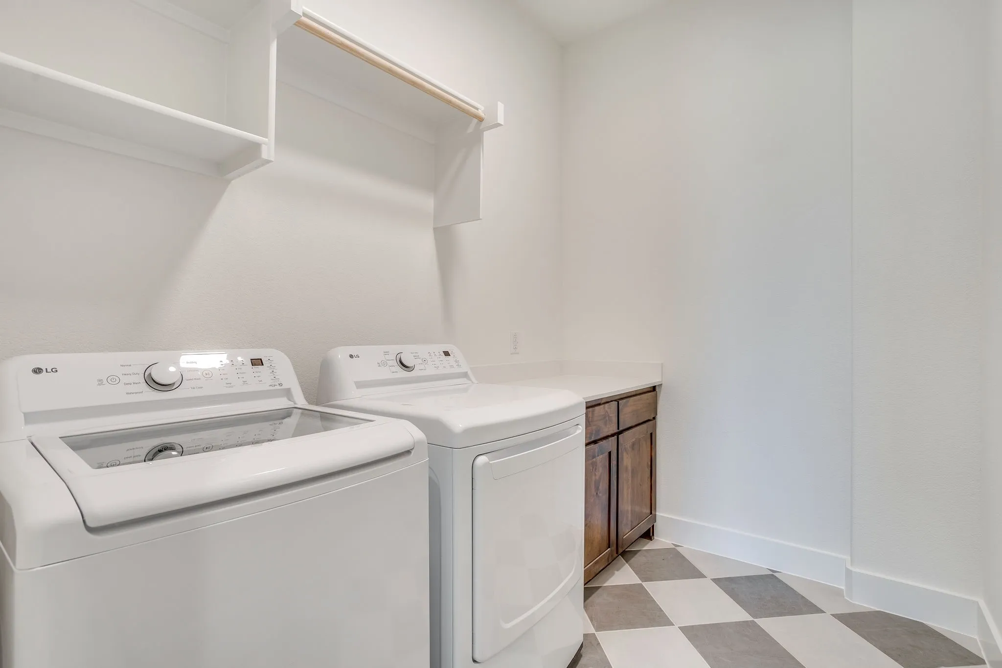 Integrated laundry area with upper shelving, a hanging rod, wood-finish cabinetry, and a light-toned countertop