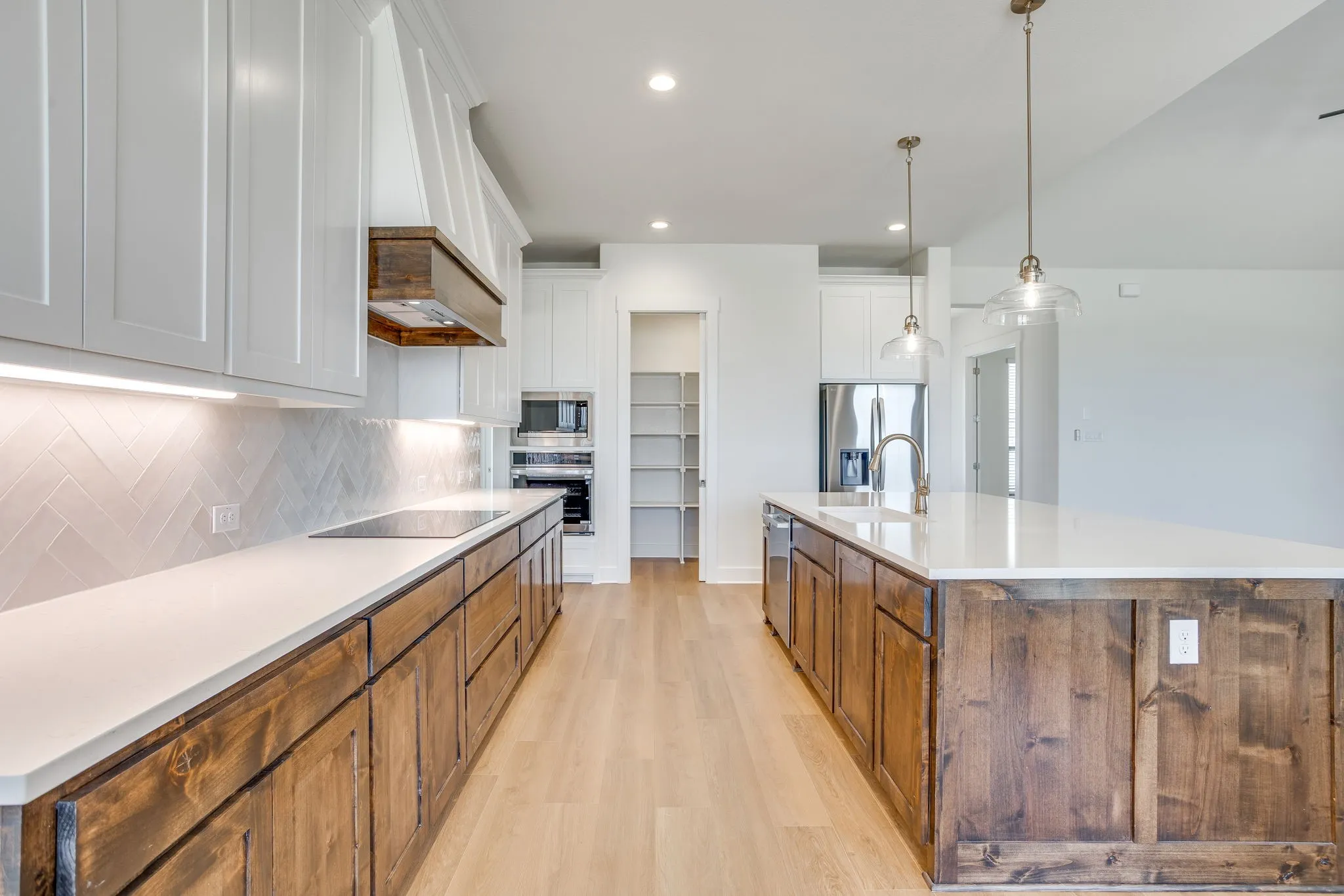 Kitchen featuring wood-finish flooring, white countertops, built-in stainless steel appliances, and a central island with a sink