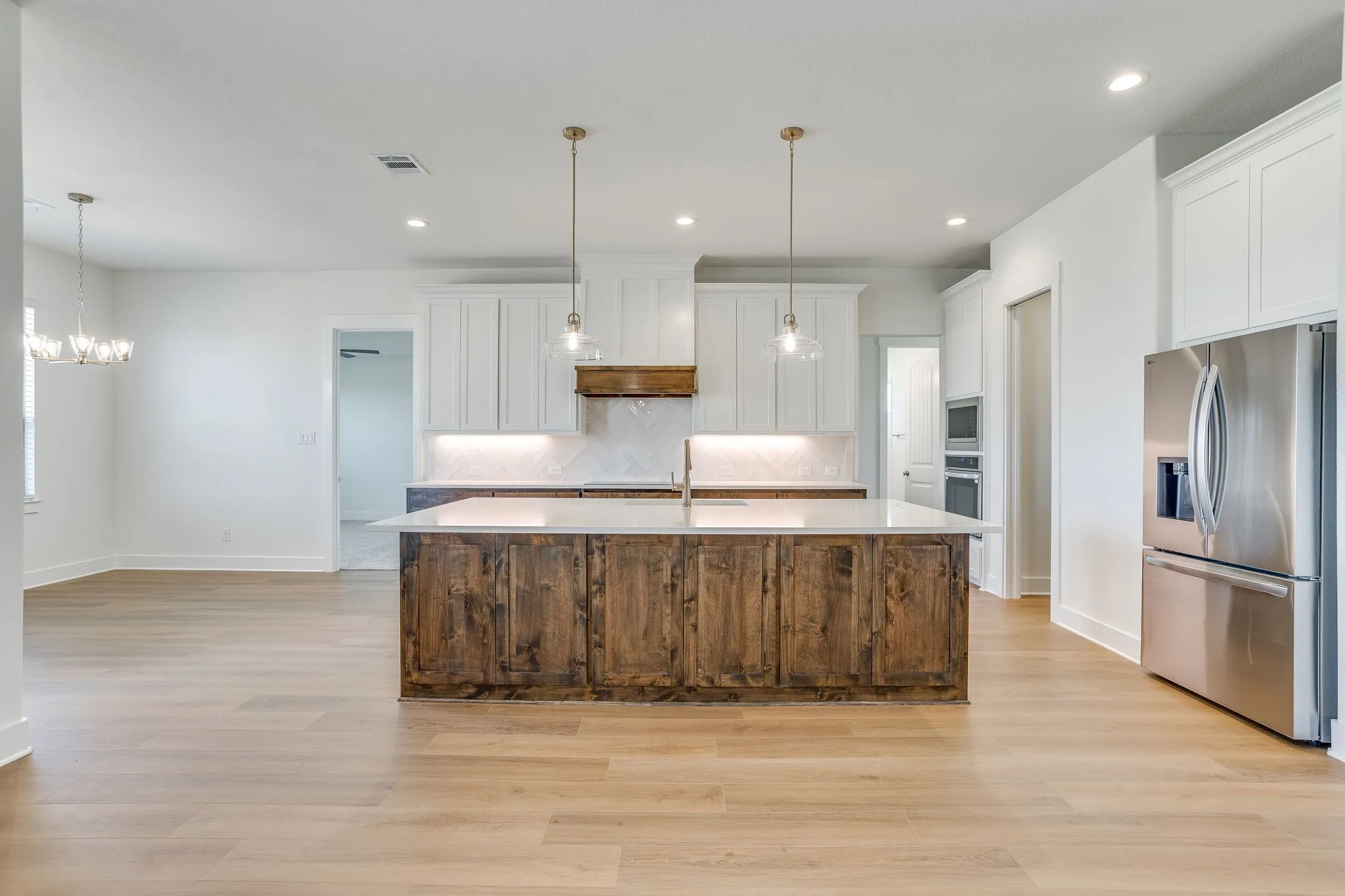 Spacious kitchen featuring an expansive center island, stainless steel appliances, white cabinetry, and wood-finish flooring