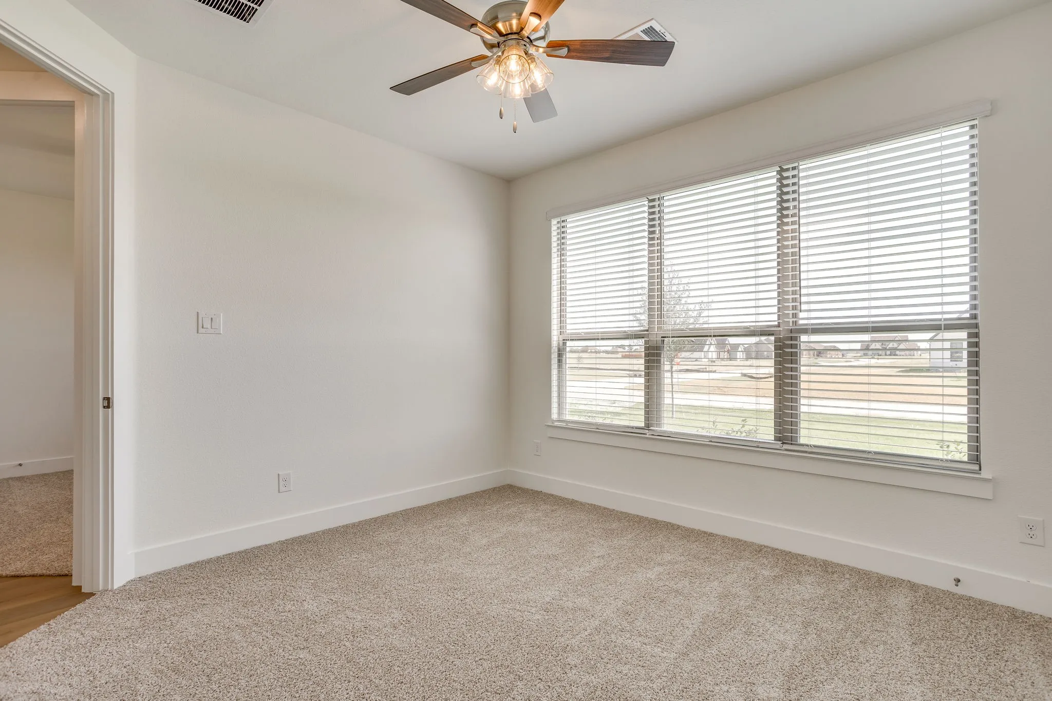 Plush carpet flooring, ceiling fan with light fixture, white walls, and a large window with blinds