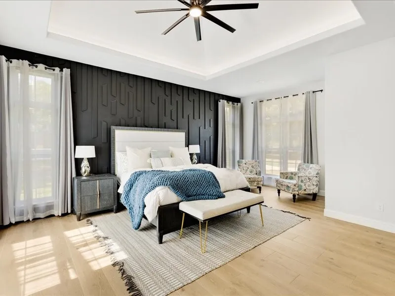 Tray ceiling with recessed lighting, ceiling fan, wood-finish flooring, accent wall with geometric paneling, and multiple windows