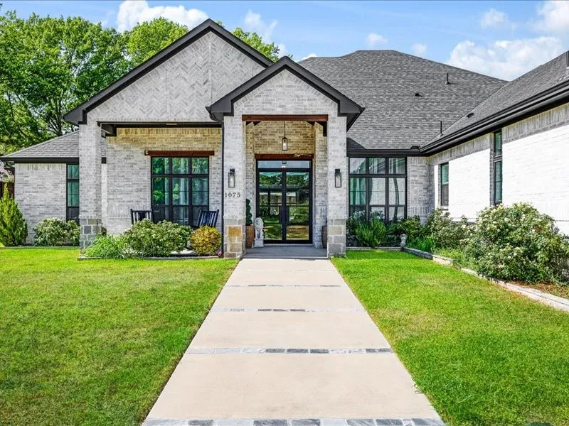 Brick exterior, dark framed windows, covered entry, patterned walkway, and established landscaping