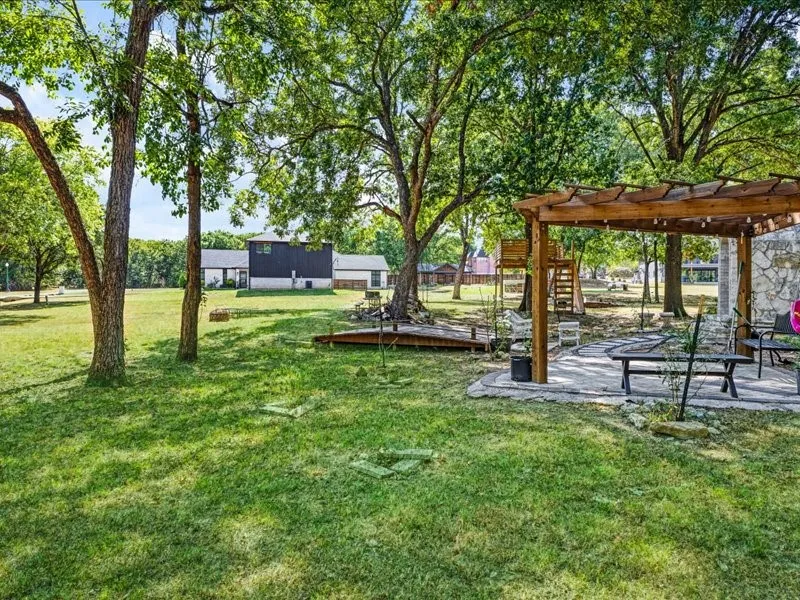 Expansive grassy yard with mature trees, a stone patio, and a wooden pergola