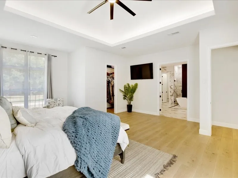 Tray ceiling with recessed lighting and a ceiling fan, wood-finish flooring, and a large window with sheer and blackout curtains