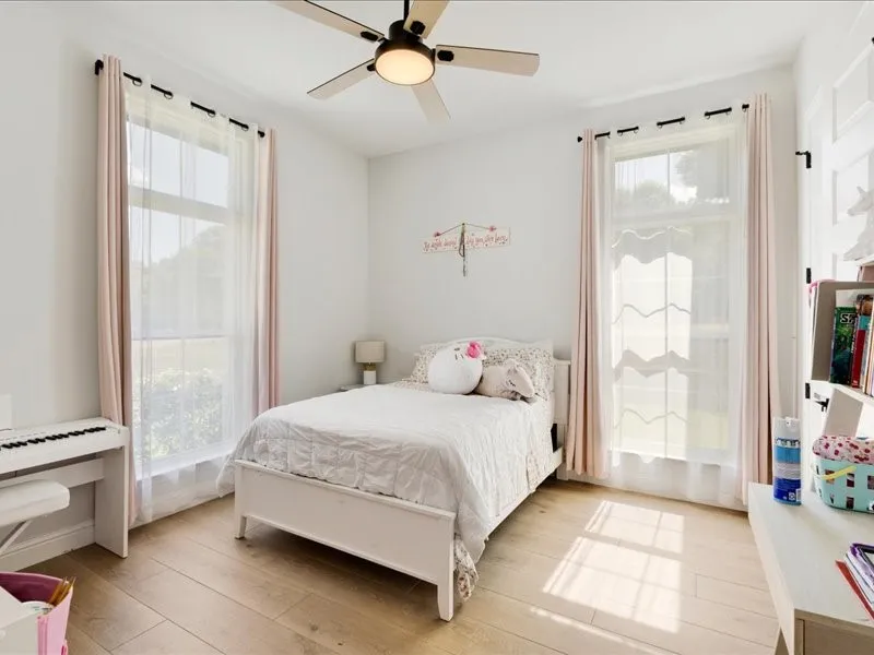 Wood-finish flooring throughout, two large windows, a ceiling fan with integrated lighting, and white walls
