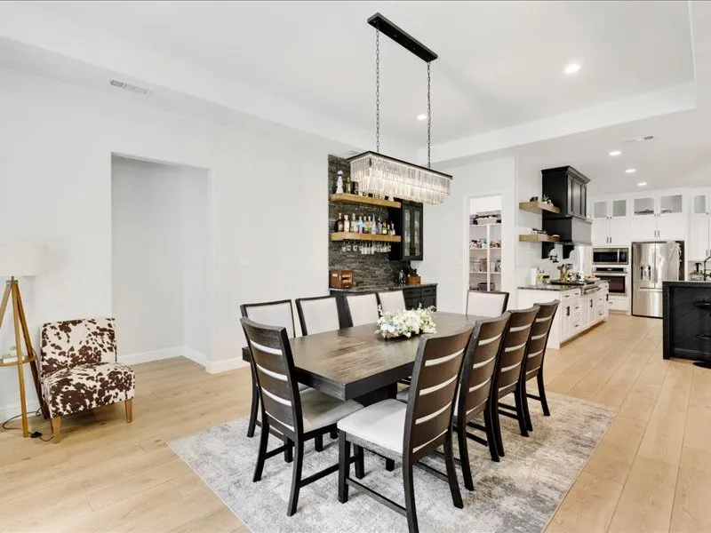Dining area featuring wood-finish flooring, a linear chandelier, and a built-in wet bar with open shelving