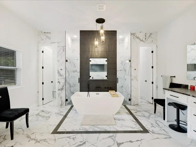 Freestanding soaking tub with a modern ceiling light fixture, large format marble-look tile flooring, and dual walk-in showers with glass enclosures