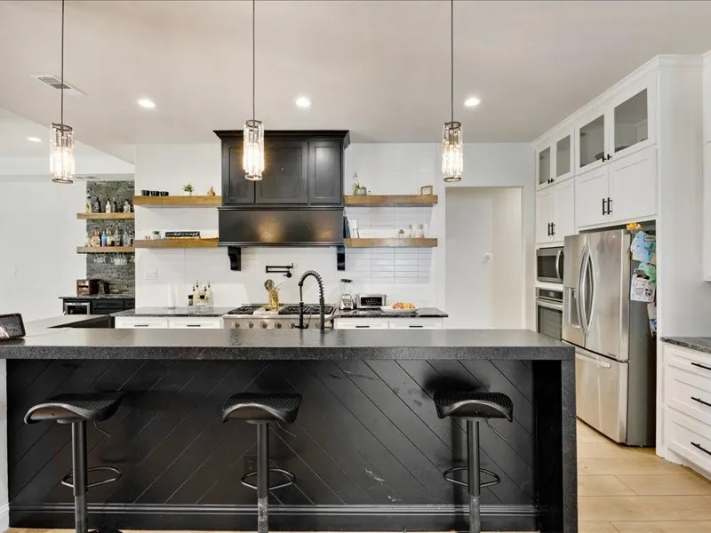 Spacious kitchen featuring an expansive island with a dark countertop and accent paneling, stainless steel appliances, white subway tile backsplash, and overhead pendant lighting
