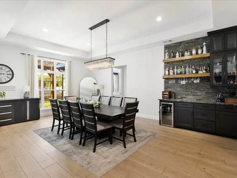 Tray ceiling, wood-finish flooring, built-in dry bar with beverage refrigerator, stacked stone accent wall, and a large window