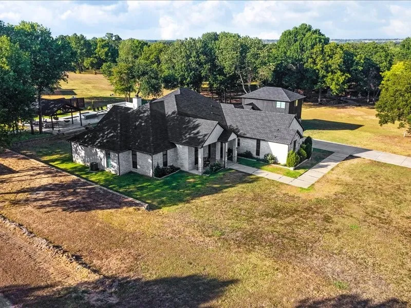 Expansive property featuring a brick exterior residence, multiple rooflines, a separate structure, an extensive driveway, and mature trees