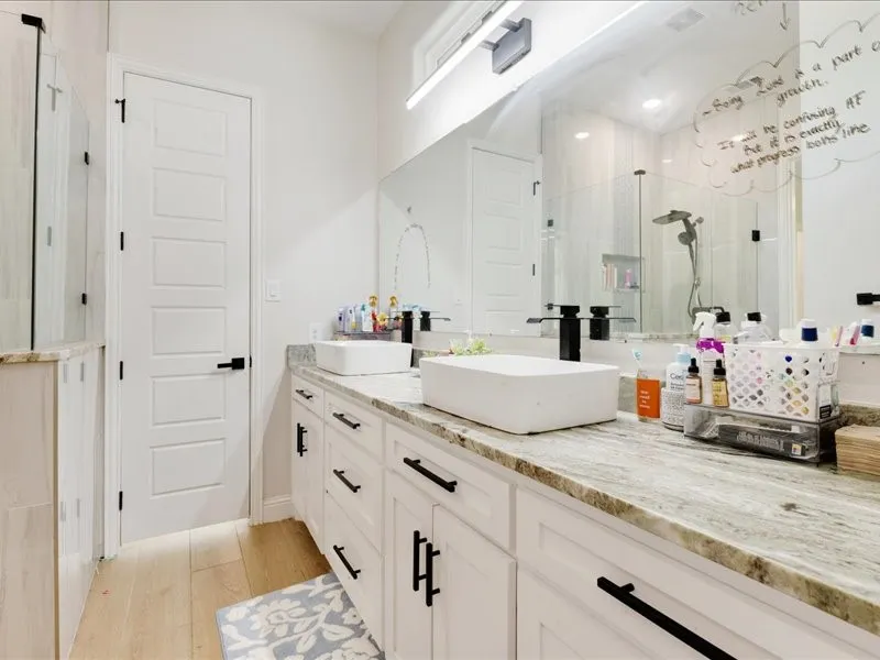 Spa-inspired primary bathroom featuring dual vessel sinks with a wood-finish vanity, stone-look countertops, and matte black hardware
