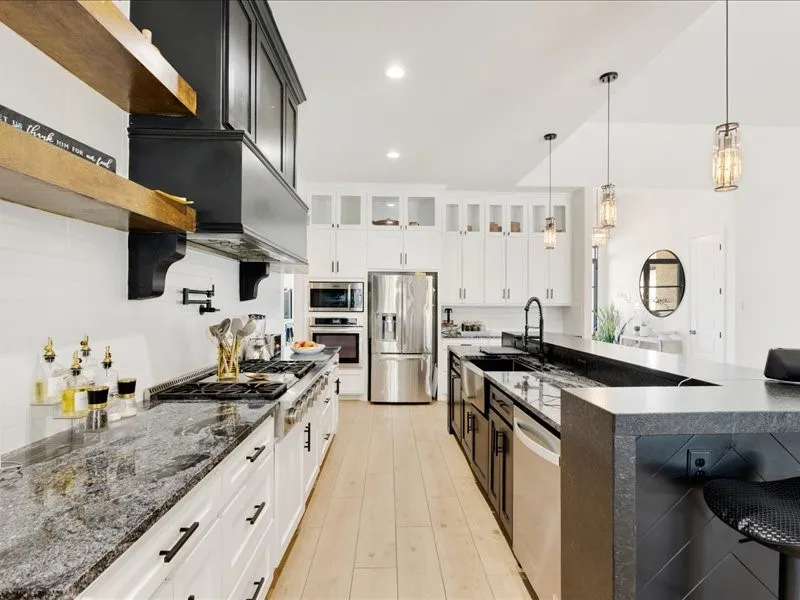 Gourmet kitchen featuring a large island, stainless steel appliances, light wood-finish flooring, white cabinetry, and pendant lighting fixtures