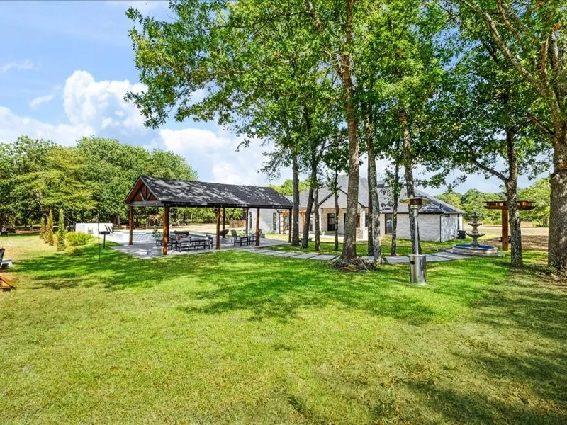 Expansive lawn with mature trees, a covered outdoor living area, a stone patio, and a tiered fountain