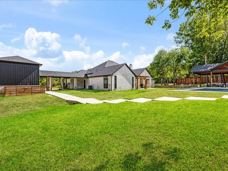 Expansive green lawn, light-colored brick exterior, dark-paneled auxiliary building, covered walkway, and outdoor pool with covered patio