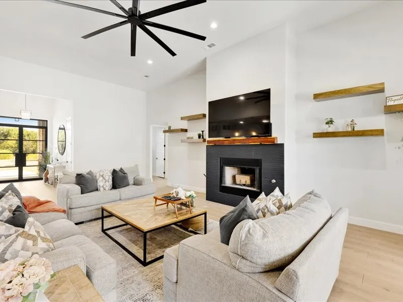 Vaulted ceilings with a large ceiling fan, light wood-finish flooring, and a fireplace with a dark tile surround and wood mantel