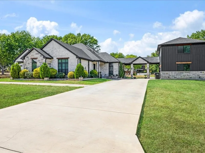 Stone and stucco exterior with dark trim accents, covered breezeway, separate outbuilding with vertical siding, and a concrete driveway