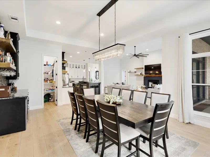 Spacious open-concept living area featuring light wood-finish flooring, a built-in wet bar with granite countertop, a walk-in pantry, and a large window with white drapery