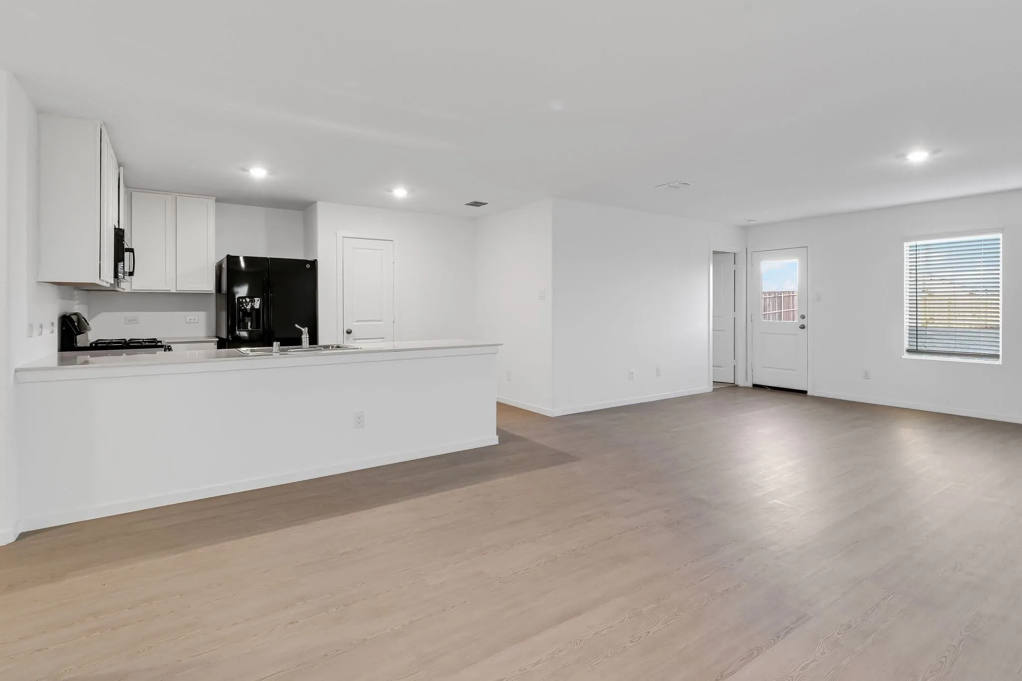 Kitchen with light wood finished floors, white cabinets, open floor plan, light countertops, and black appliances