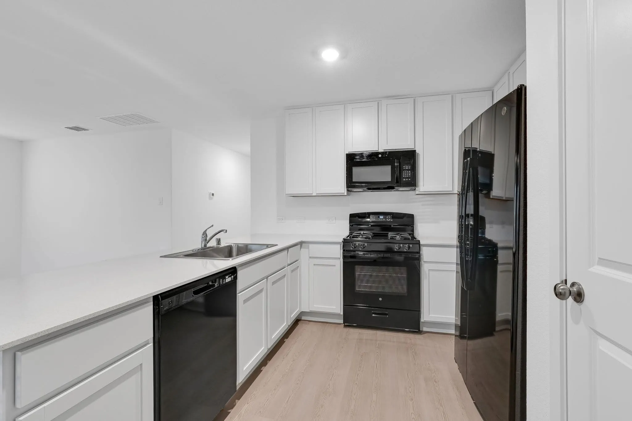 Kitchen with light countertops, visible vents, white cabinets, a sink, and black appliances