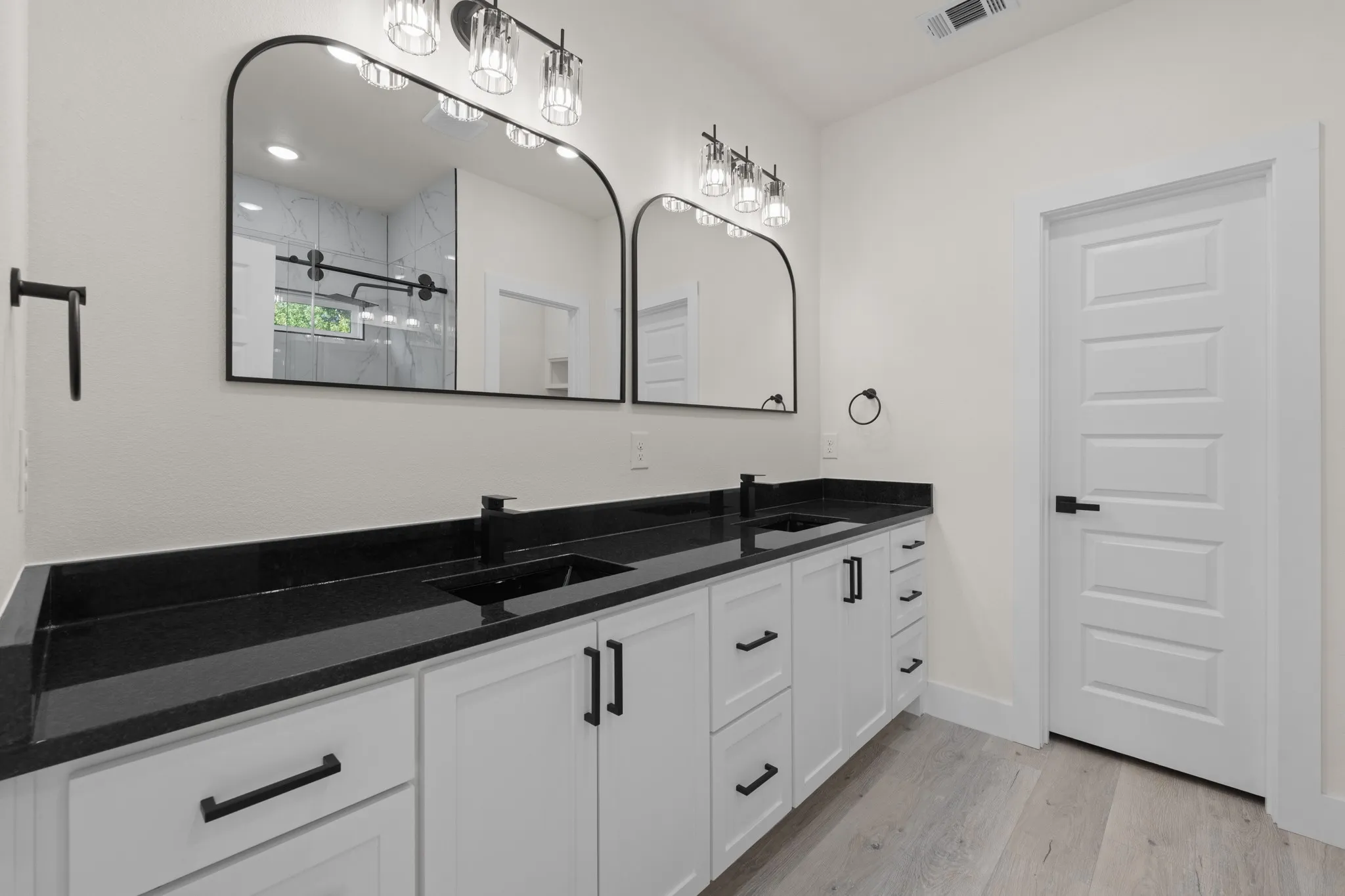 Dual arched mirrors, black countertop, white cabinetry, black hardware, wood-finish flooring
