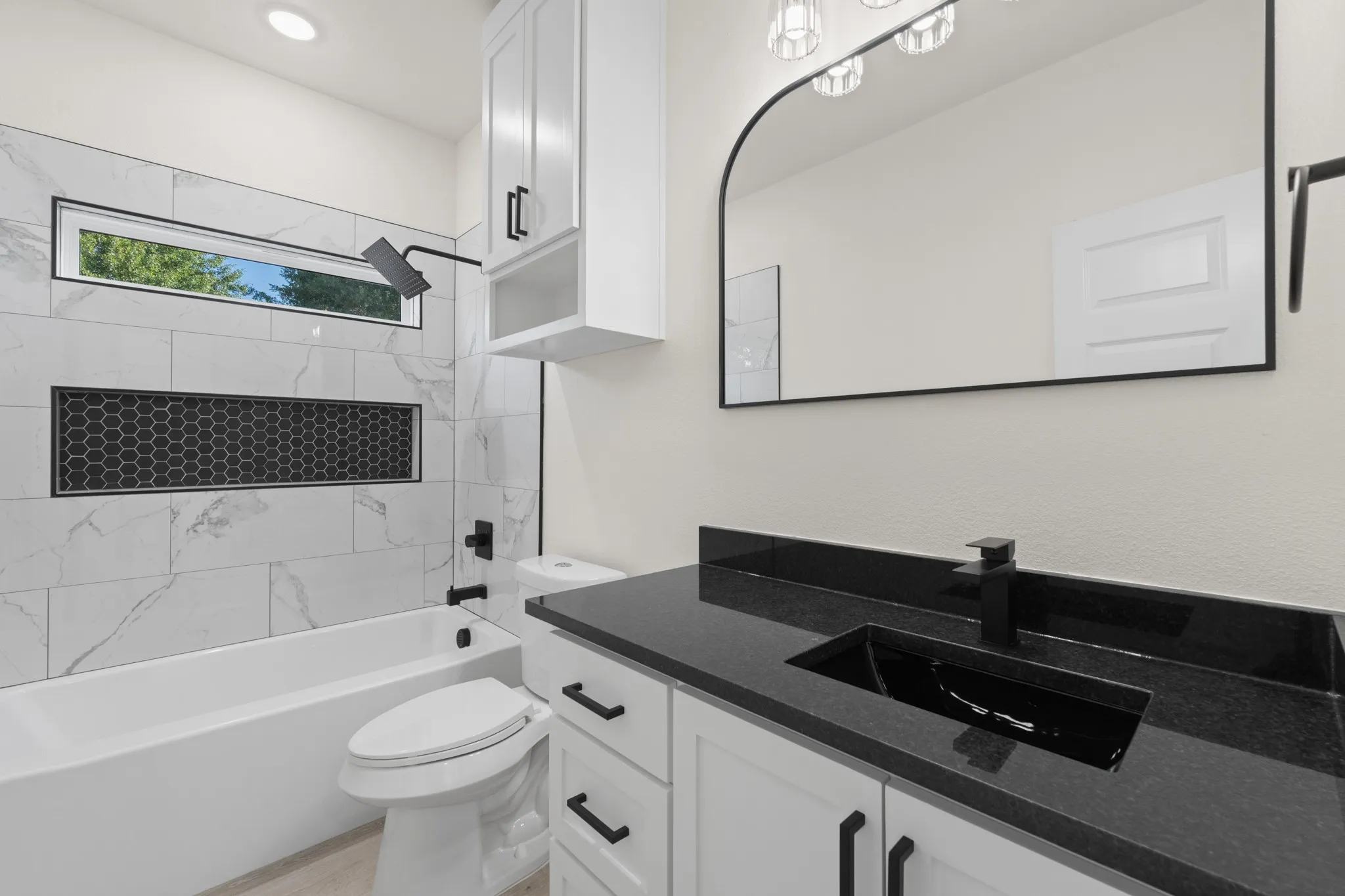 White tile shower surround with a black honeycomb accent niche, a horizontal window, and matte black fixtures