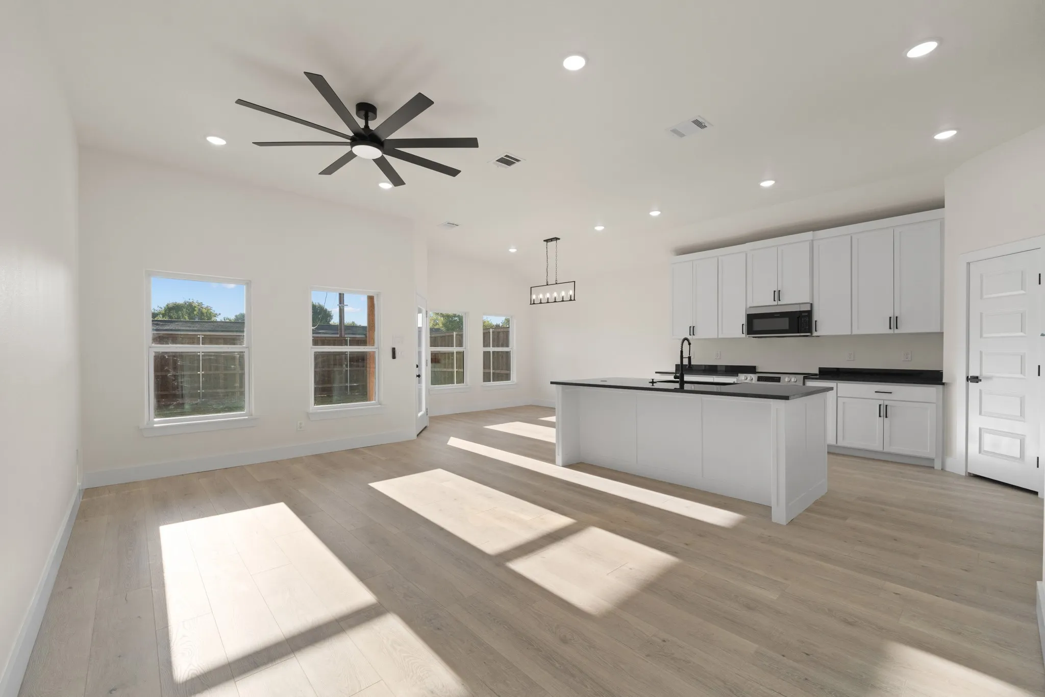 Open-concept living space featuring wood-finish flooring, recessed lighting, a vaulted ceiling, and a modern kitchen with a center island and white cabinetry