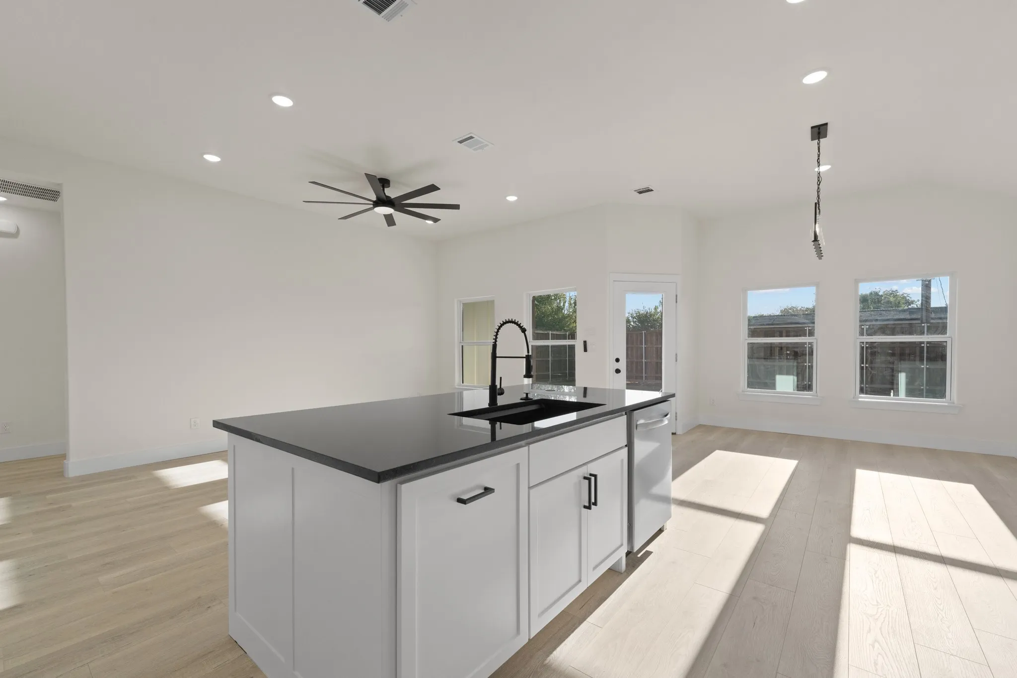 Kitchen island with a dark countertop and undermount sink, white cabinetry with black hardware, wood-finish flooring, and recessed lighting