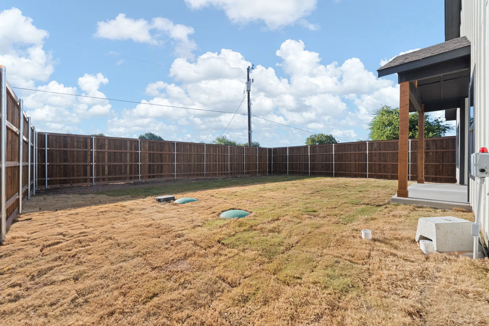 Expansive backyard featuring a wood privacy fence, covered patio, and concrete slab