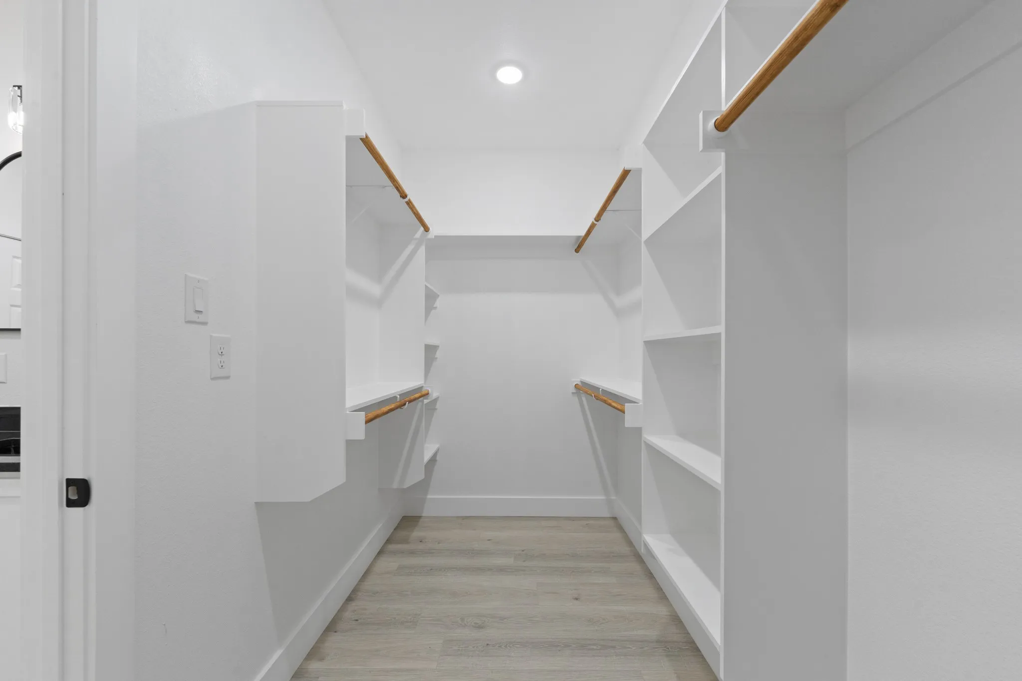 Walk-in closet with integrated shelving, wood-finish hanging rods, recessed lighting, and light-toned wood-finish flooring