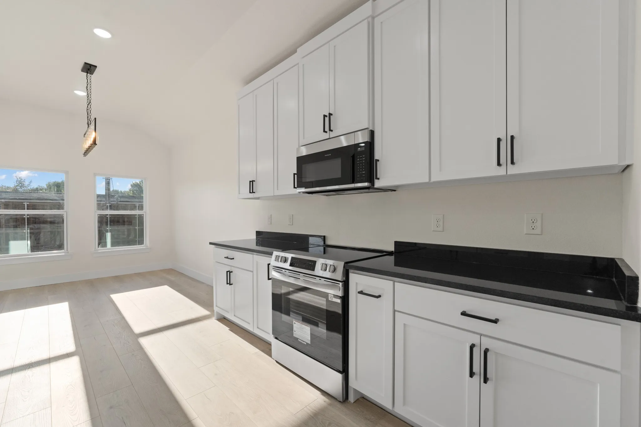 Kitchen featuring white shaker-style cabinetry, dark countertops, stainless steel appliances, and wood-finish flooring