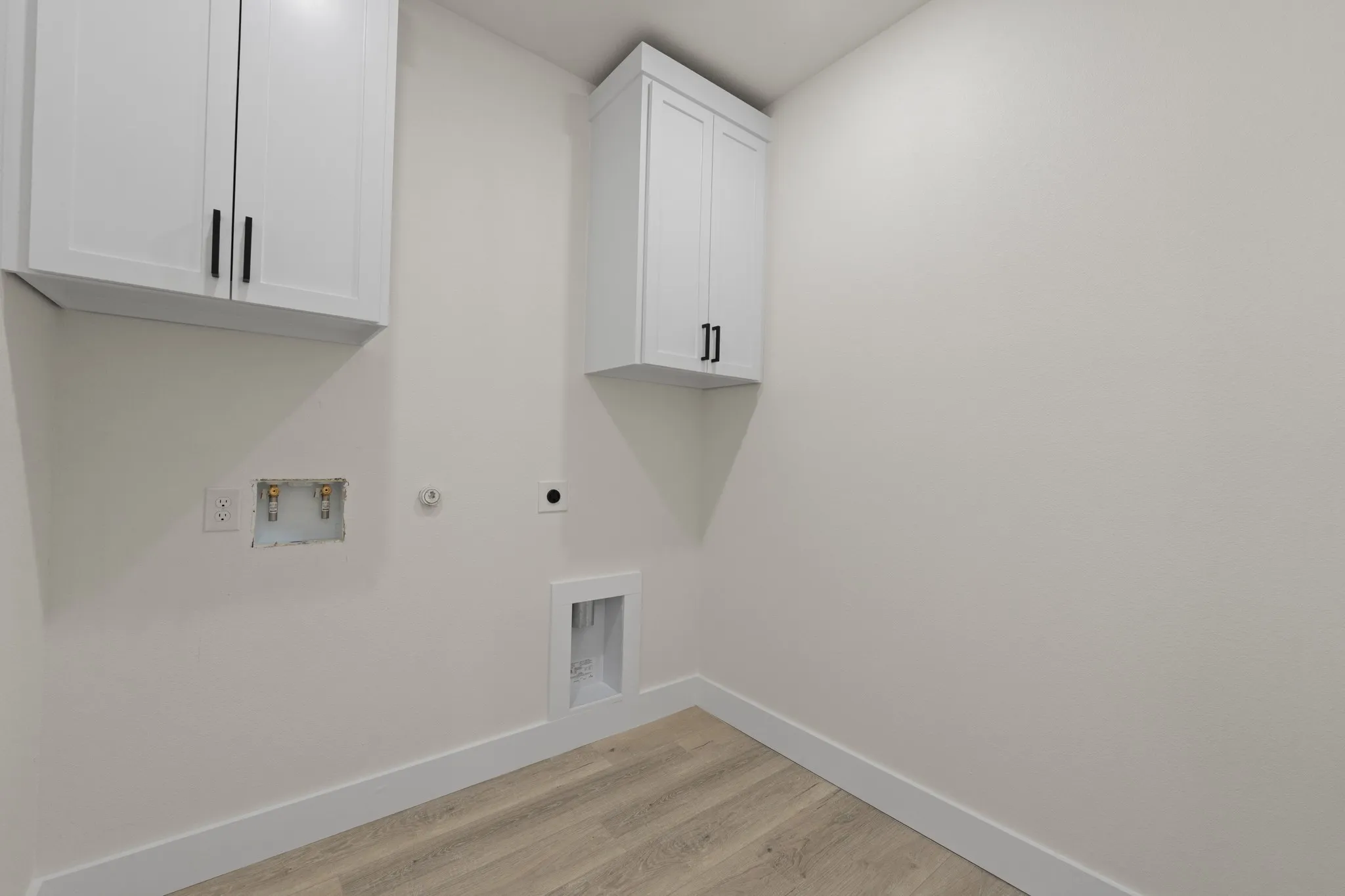 White shaker cabinetry with black hardware, light wood-finish flooring, and crisp white walls