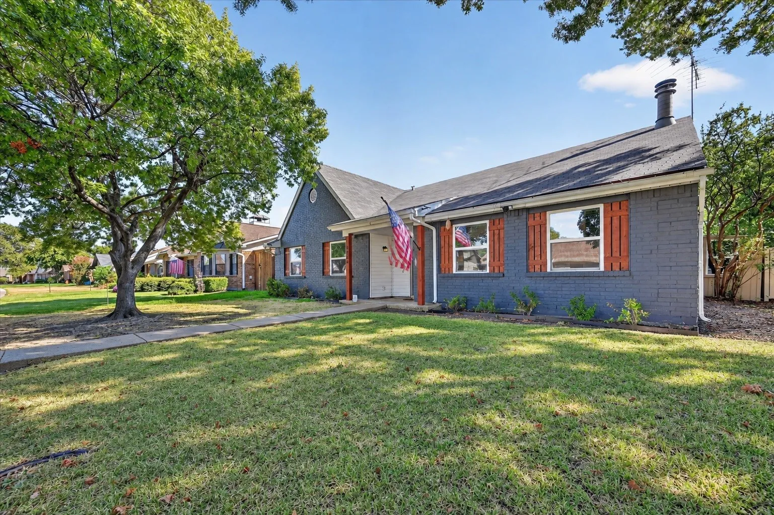 Brick exterior with a peaked roofline, featuring decorative window shutters, a front porch, and mature trees