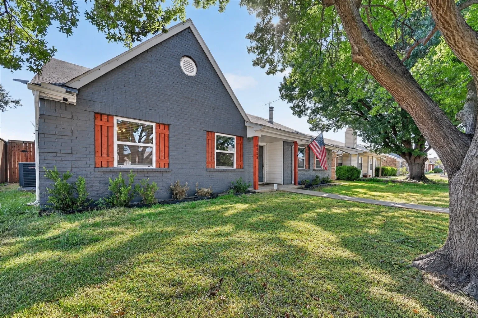 Charcoal gray brick exterior with white trim, red wooden shutters, and a prominent front gable