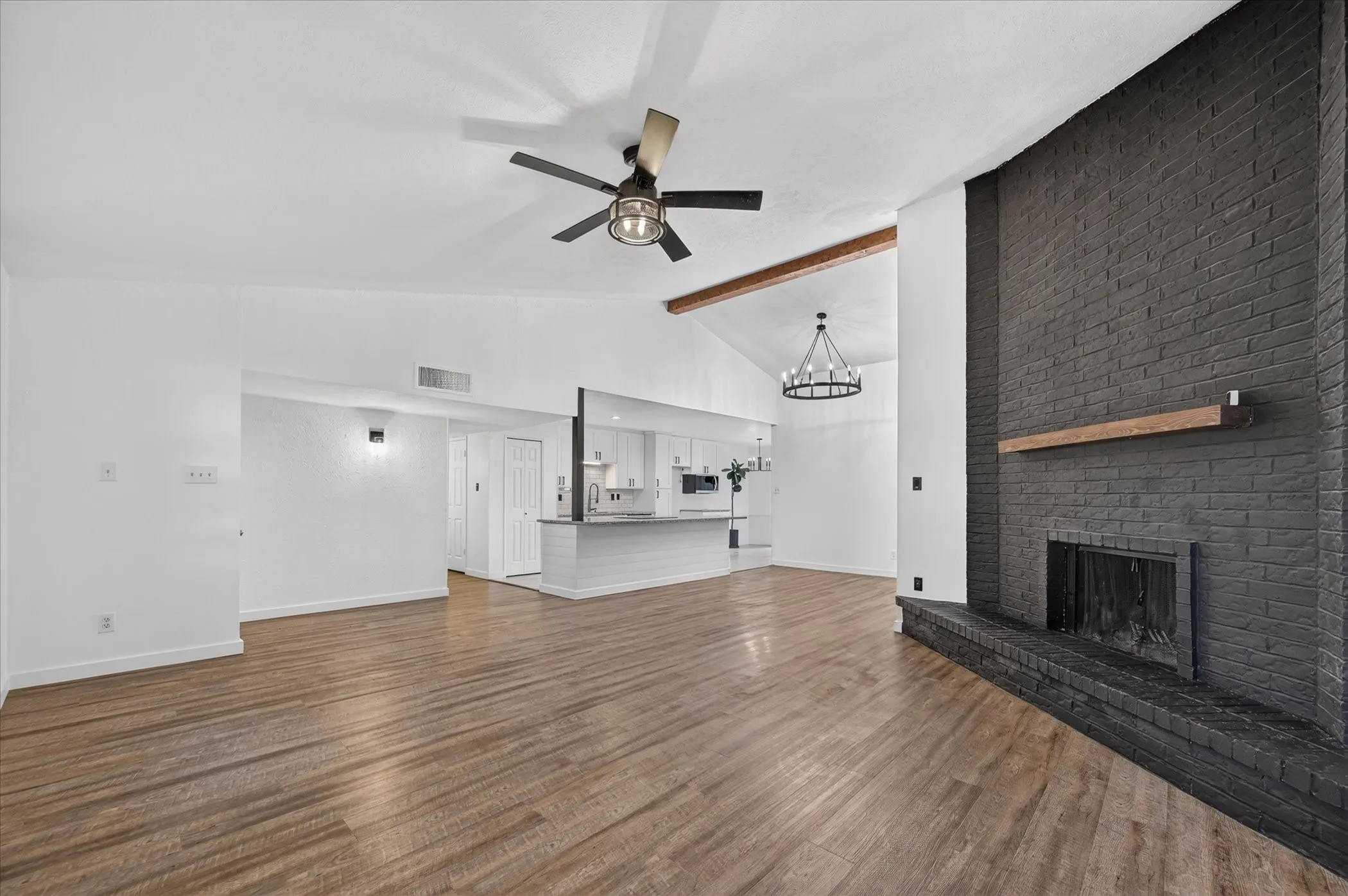 Spacious living area featuring wood-finish flooring, a vaulted ceiling with exposed beam, and a ceiling fan