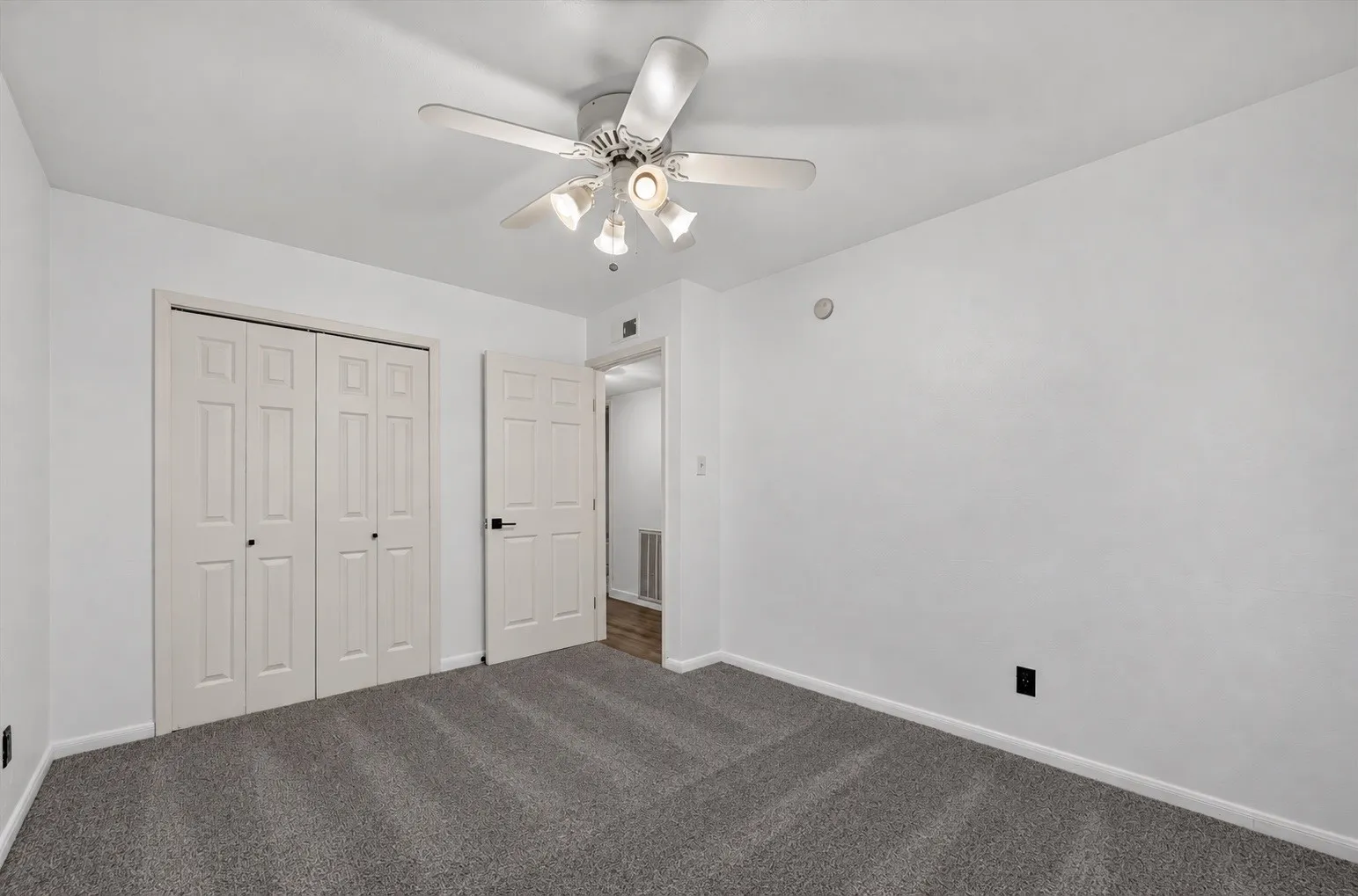 Bedroom with plush gray carpeting, white walls, a ceiling fan with integrated lighting, and bi-fold closet doors