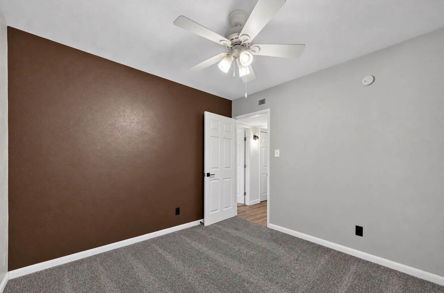 Textured accent wall, ceiling fan with integrated lighting, paneled interior doors, and gray carpet flooring
