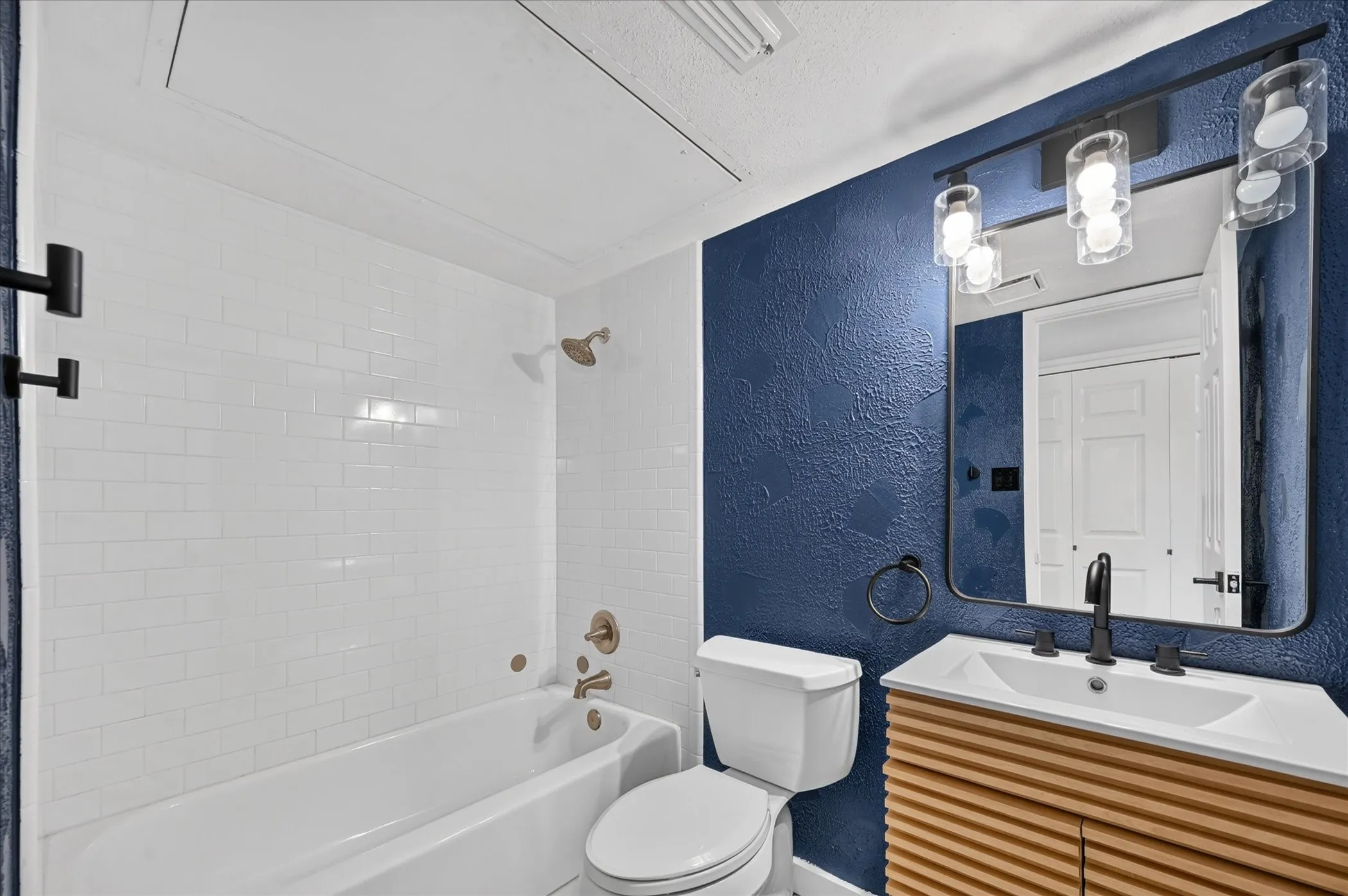 White subway tile shower surround, integrated bathtub, and a wood-finish vanity with a white basin sink