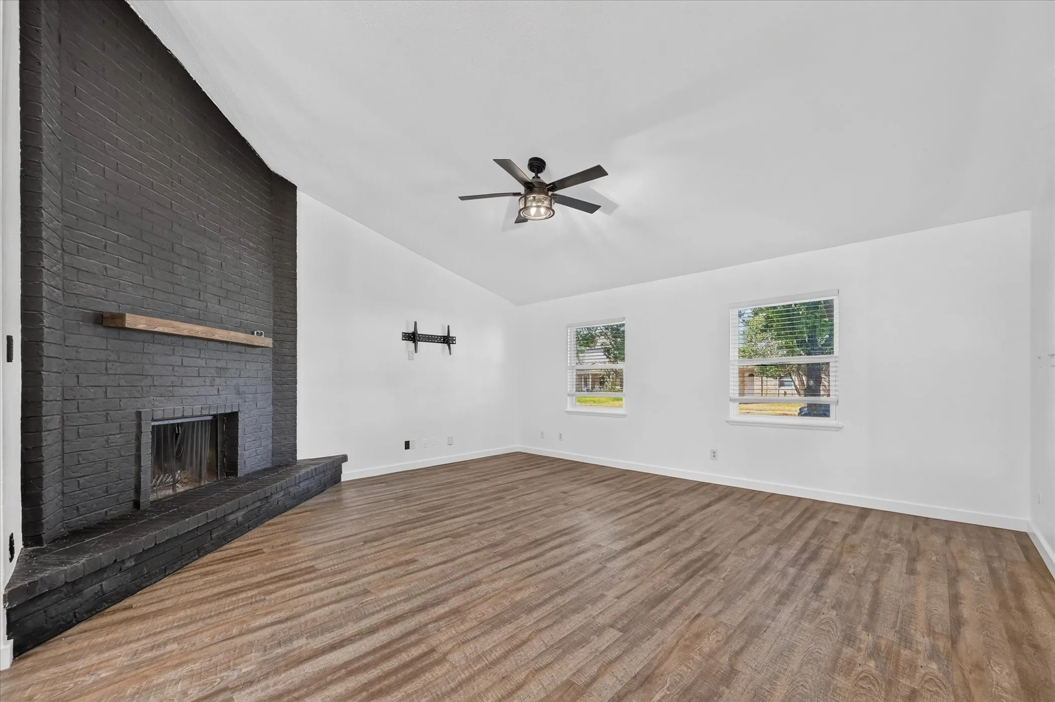 Expansive living area with wood-finish flooring, a painted brick fireplace, and a light wood mantel