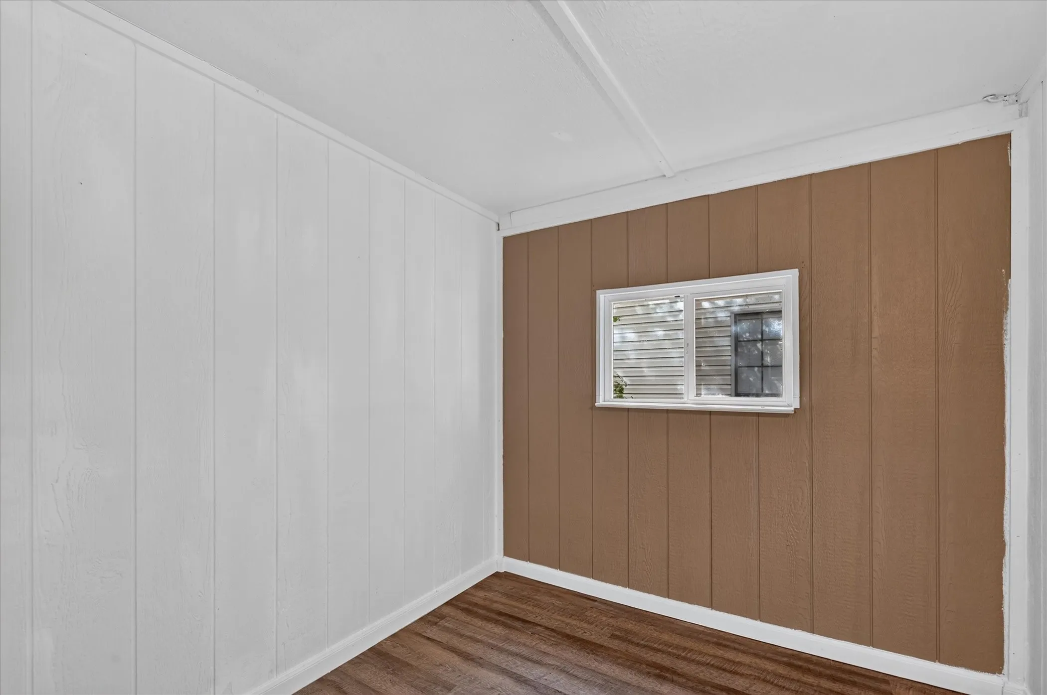 Wood-finish flooring with white baseboards, a white paneled wall, and a brown paneled accent wall with a window