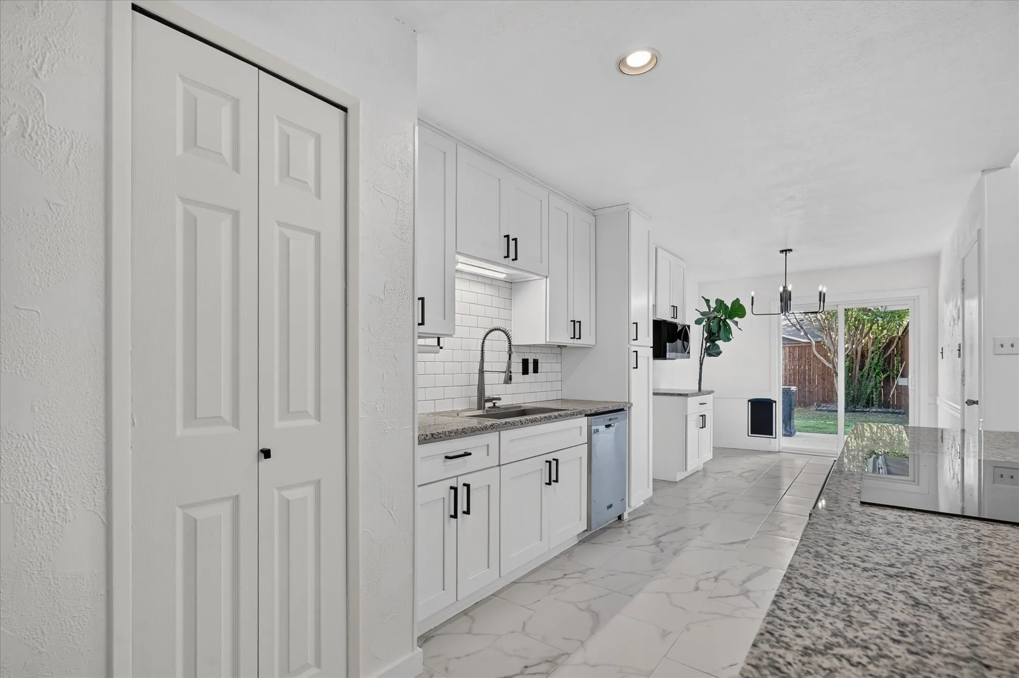 White shaker cabinetry, stone countertops, subway tile backsplash, stainless steel sink with gooseneck faucet, and white wood-finish flooring