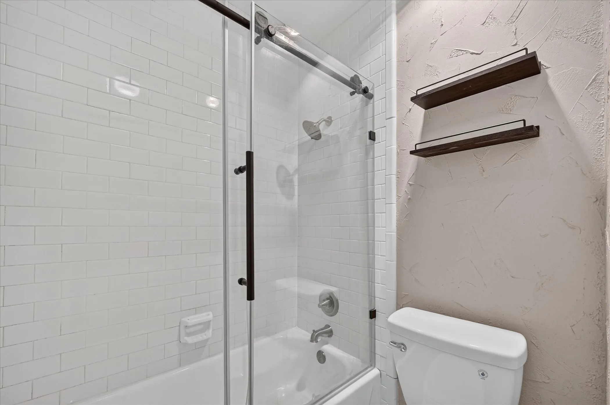 White subway tile surround with a glass-enclosed shower and tub combination, featuring matte black hardware