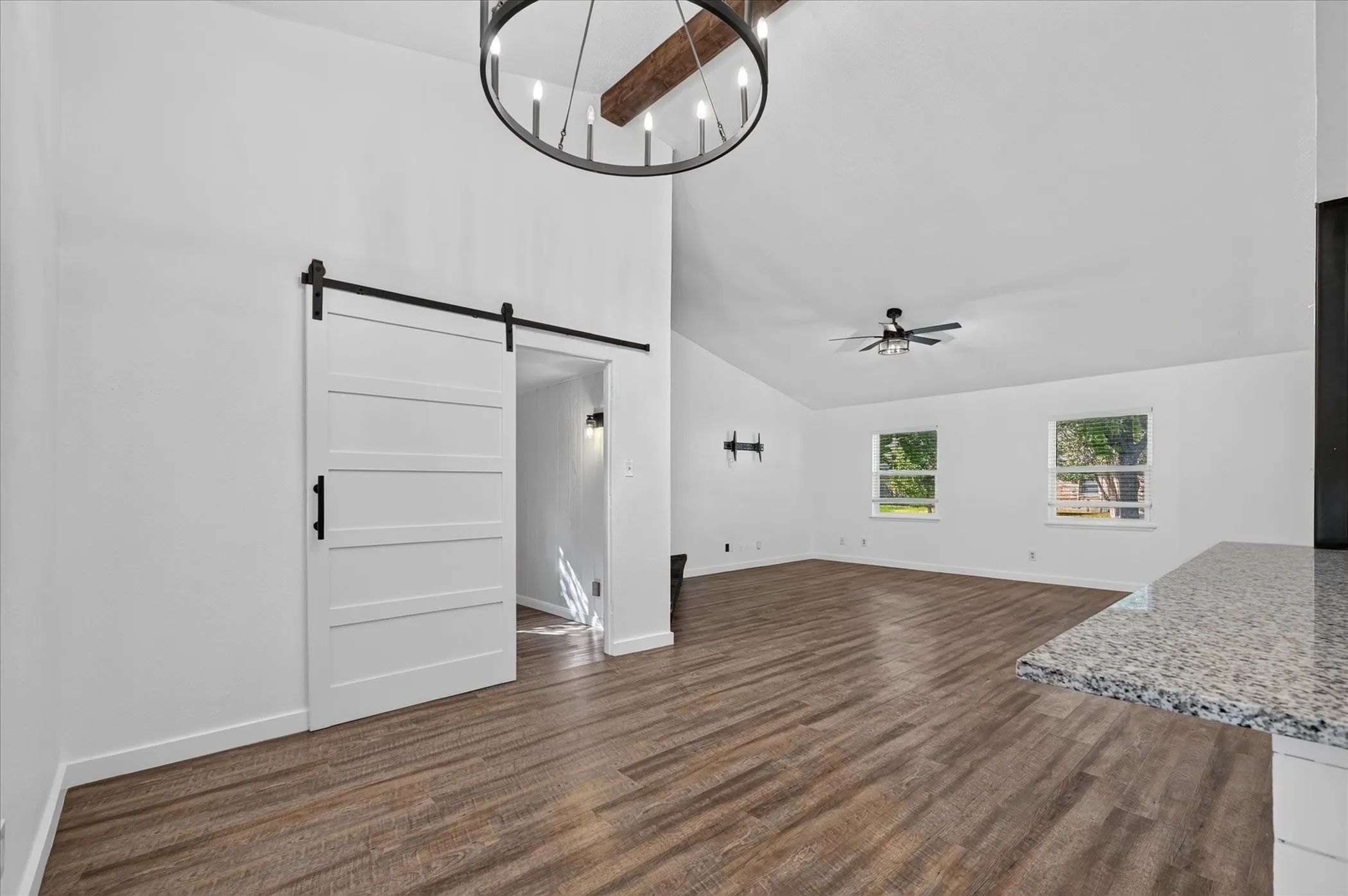 Vaulted ceiling featuring a large chandelier, wood-finish flooring, and white barn door