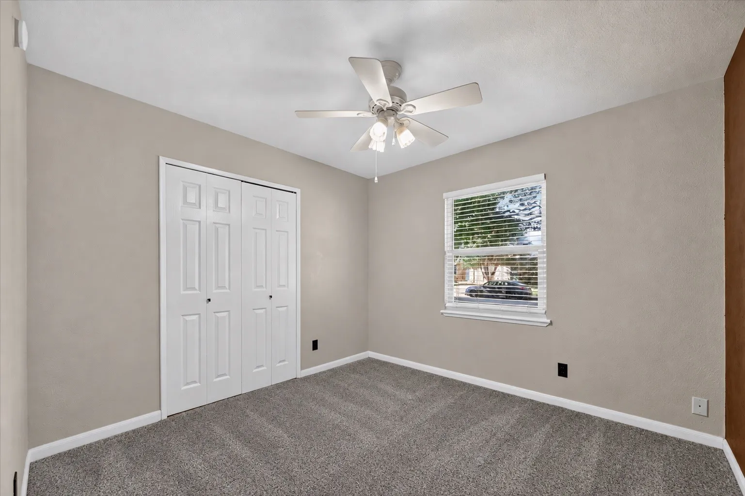 Plush gray carpeting, a ceiling fan with integrated lighting, and a white window with blinds
