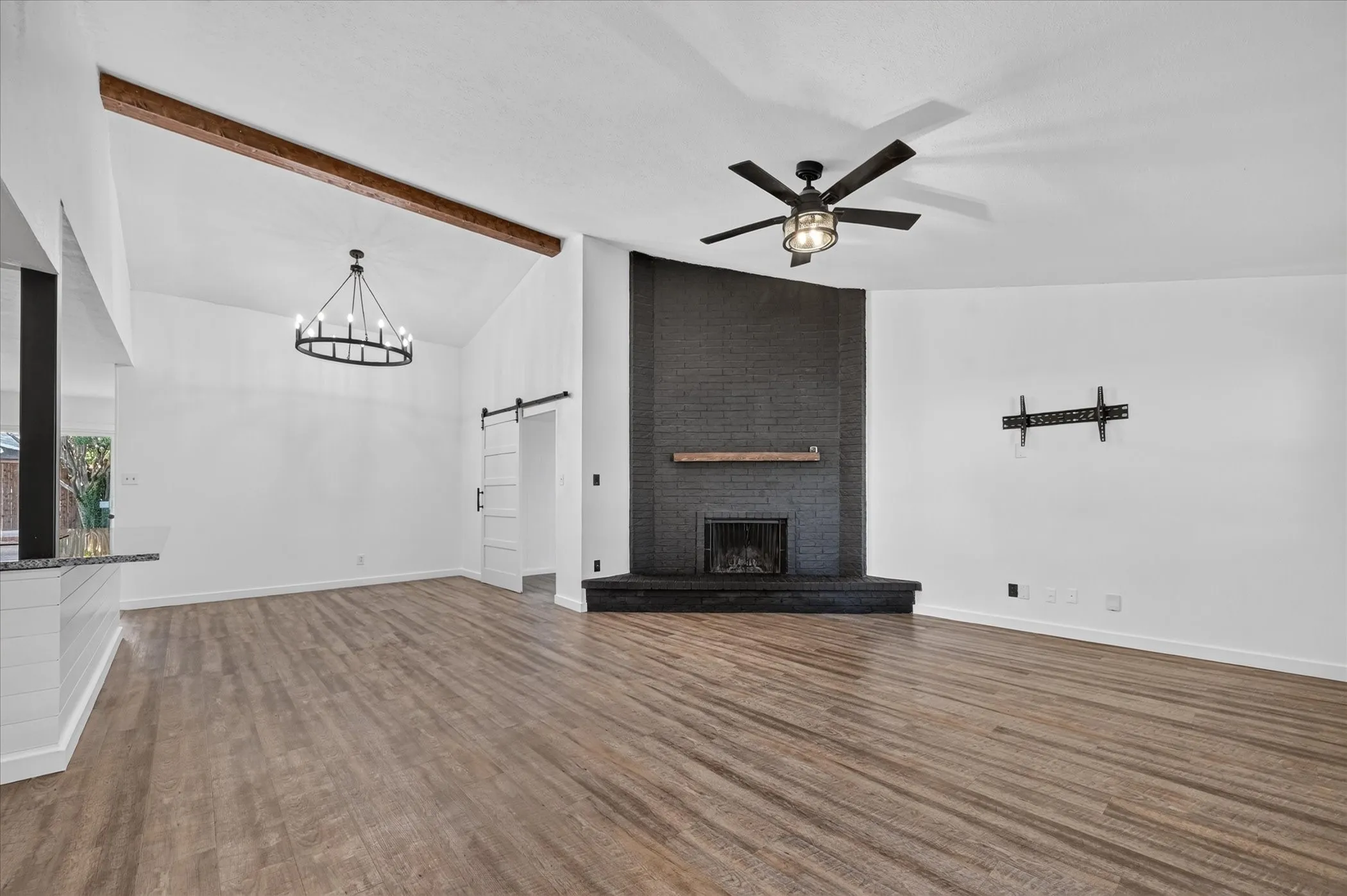 Vaulted ceiling with exposed wood beam, black brick fireplace with wood mantel, wood-finish flooring, and a modern chandelier