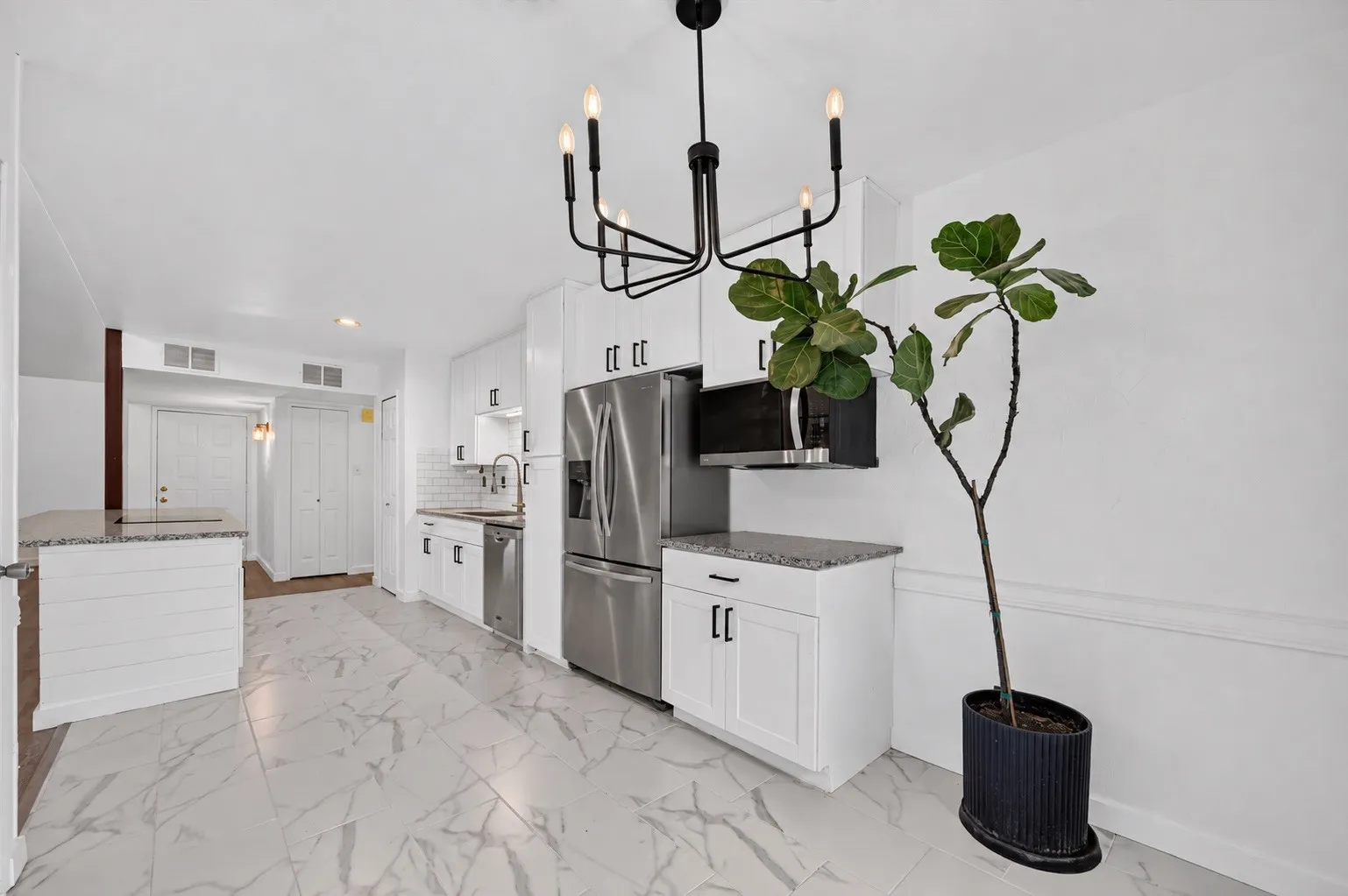White cabinetry with matte black hardware, stainless steel appliances, granite countertops, white subway tile backsplash, and large format marble-look floor tiles