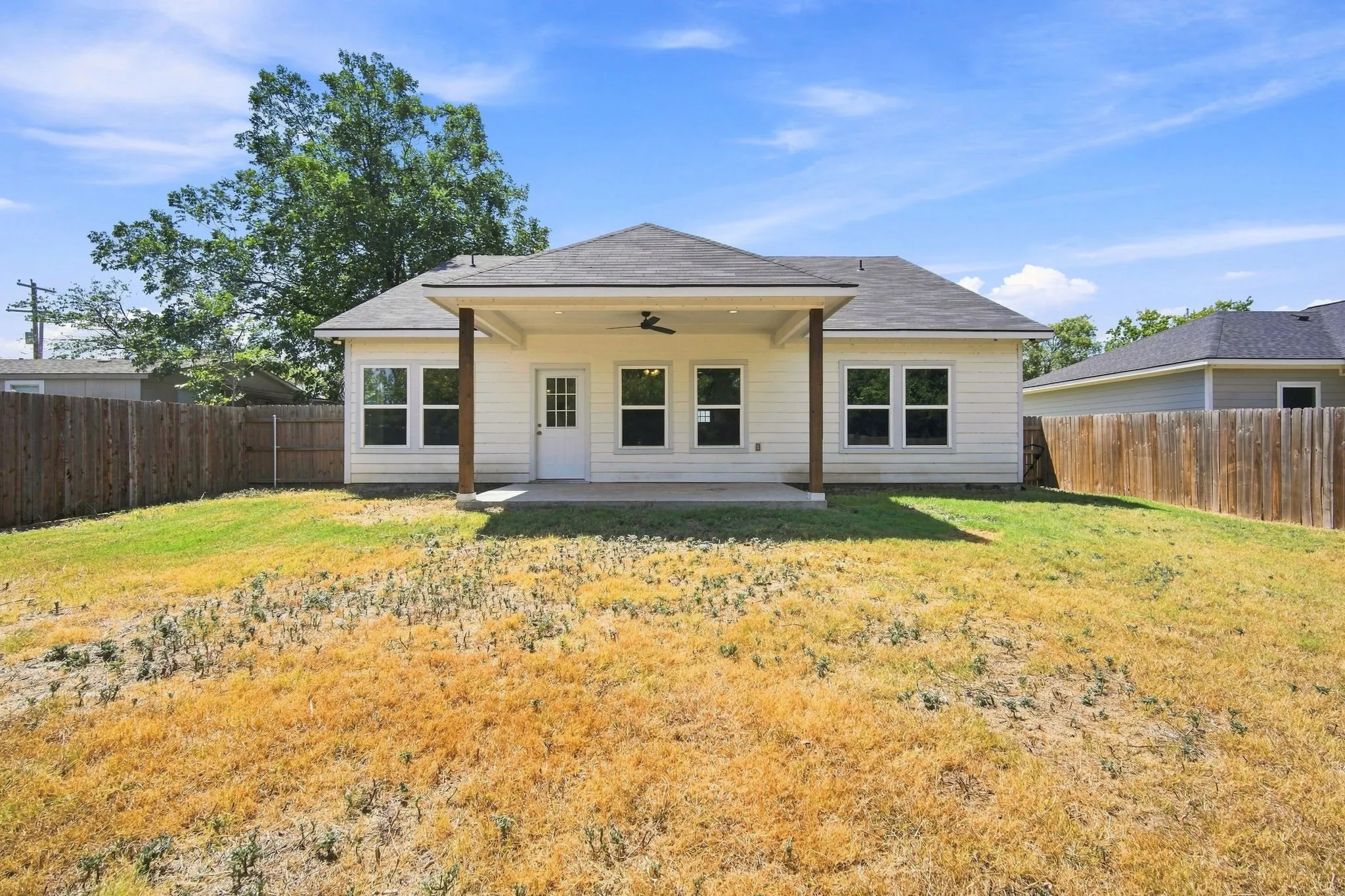 Rear exterior featuring a covered patio with an outdoor ceiling fan, multiple windows, and a privacy fence