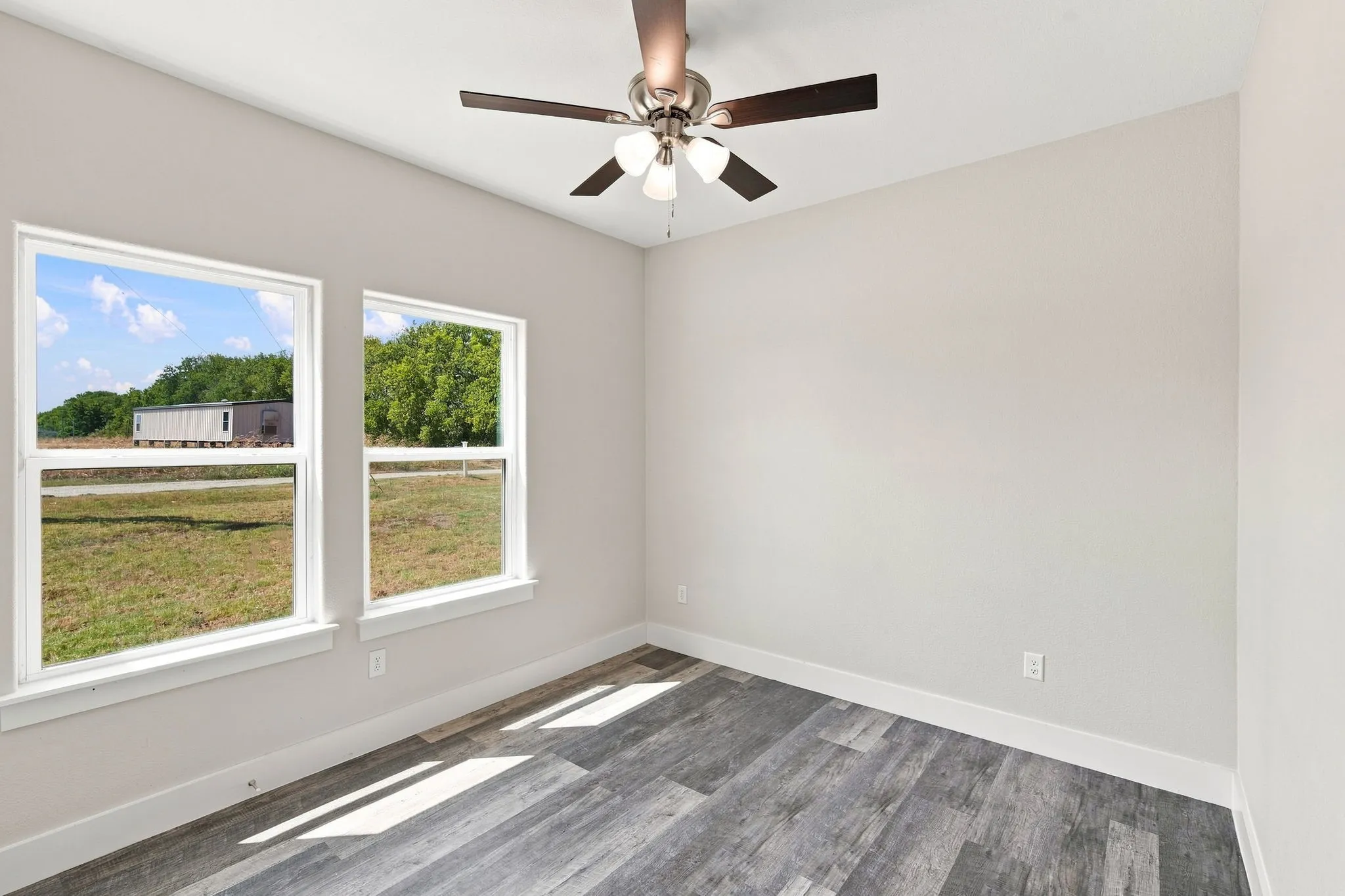 Two windows, wood-finish flooring, and an overhead ceiling fan with lighting