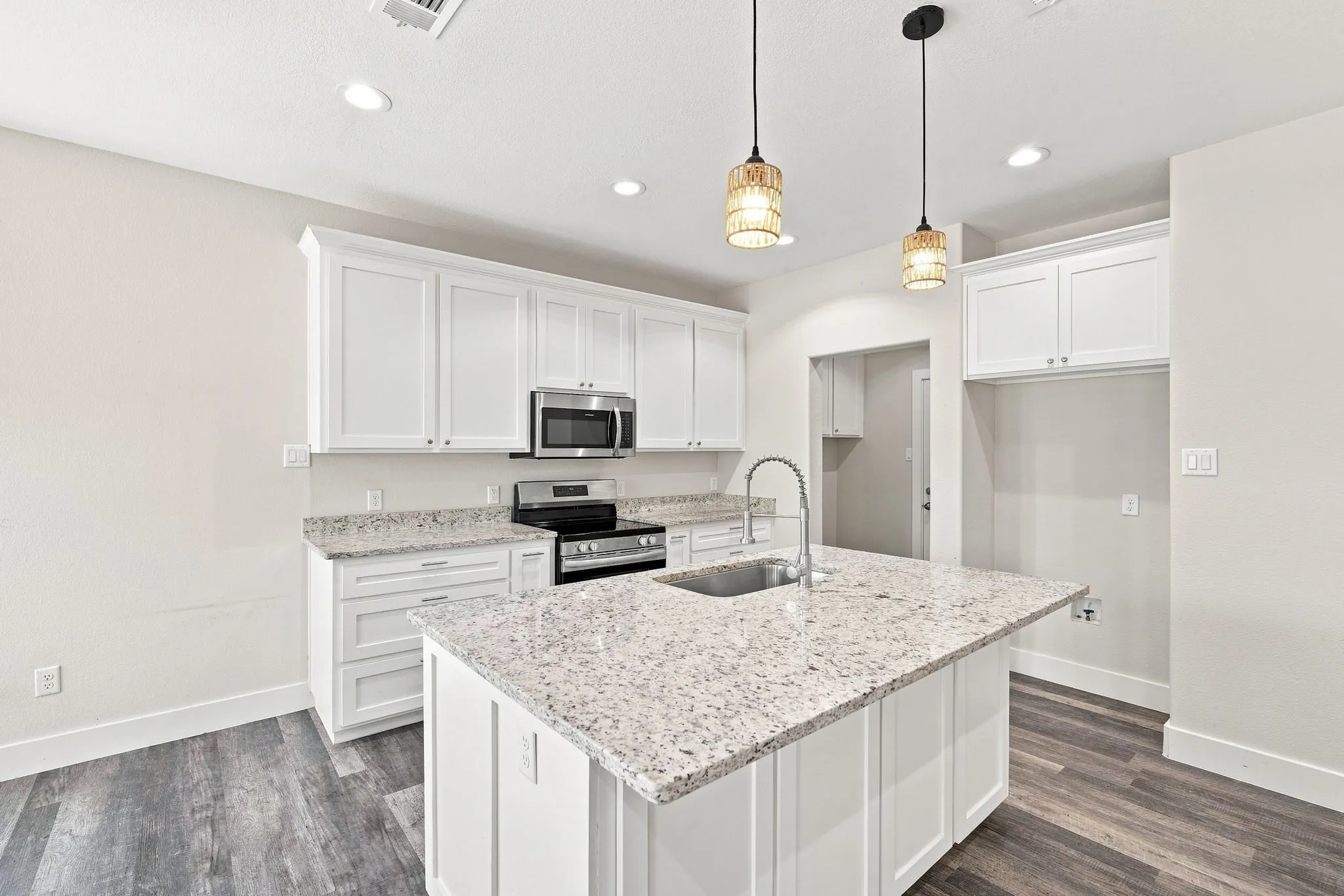 Modern kitchen featuring white shaker cabinetry, stainless steel appliances, speckled stone countertops, and wood-finish flooring